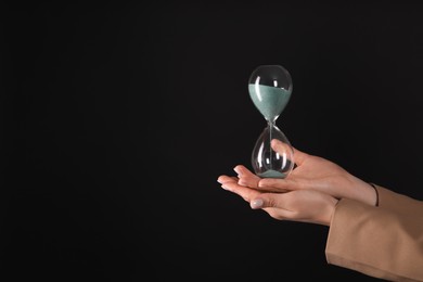 Businesswoman holding hourglass on black background, closeup with space for text. Time management