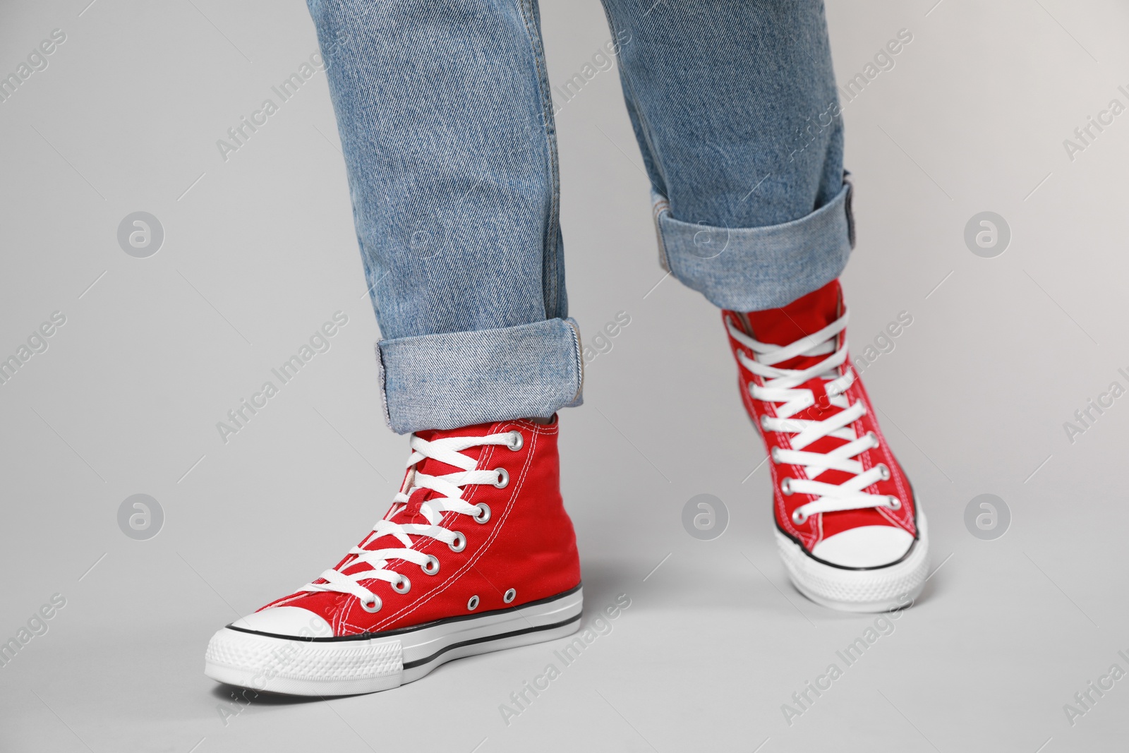 Photo of Woman wearing pair of new stylish sneakers on light grey background, closeup