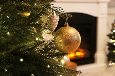 Photo of Beautiful Christmas ball hanging on fir tree branch in room, closeup