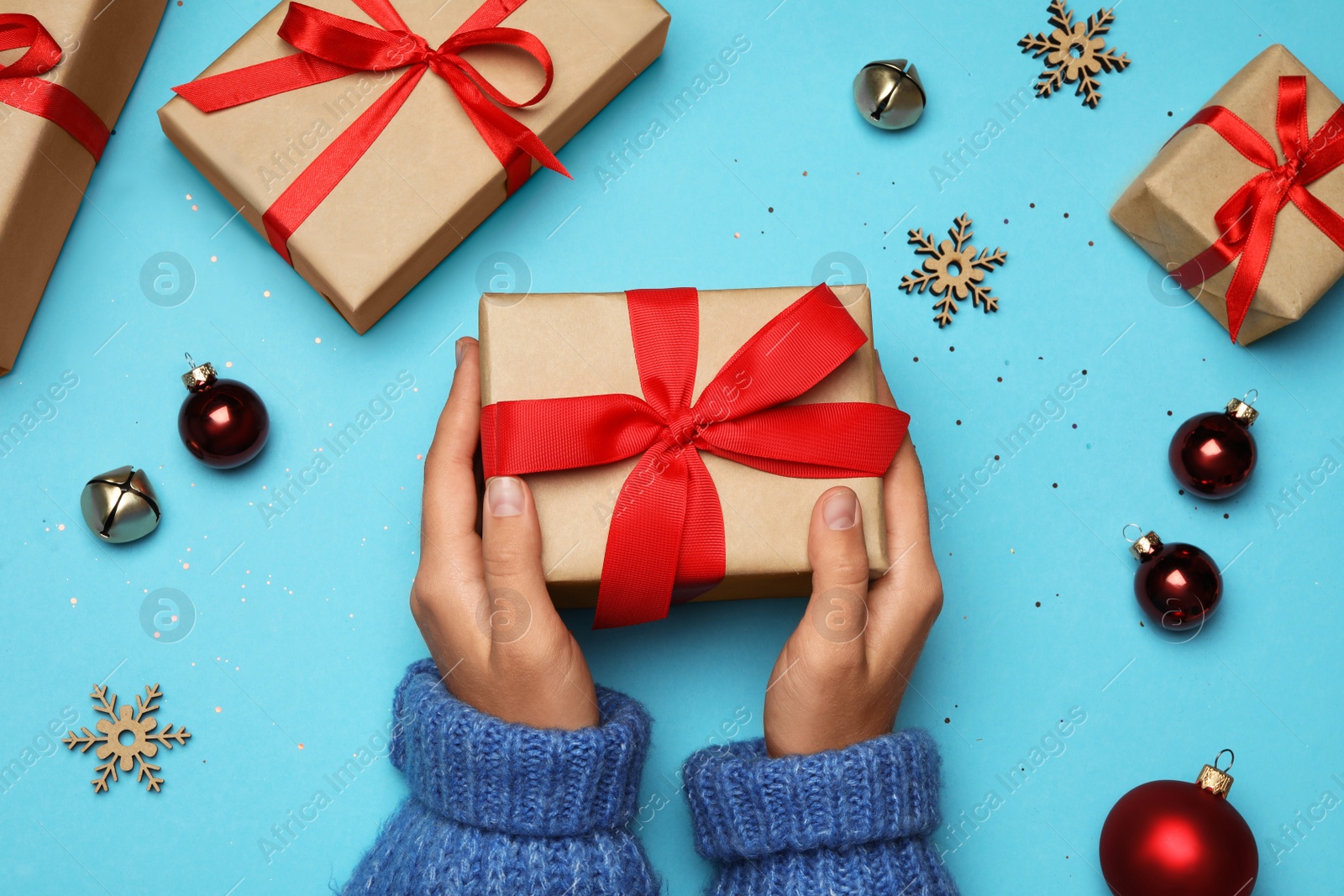 Photo of Young woman holding Christmas gift on light blue background, flat lay