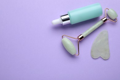 Photo of Gua sha stone, face roller and bottle of serum on violet background, flat lay. Space for text
