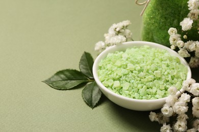 Photo of Bowl with sea salt and beautiful flowers on olive background. Space for text