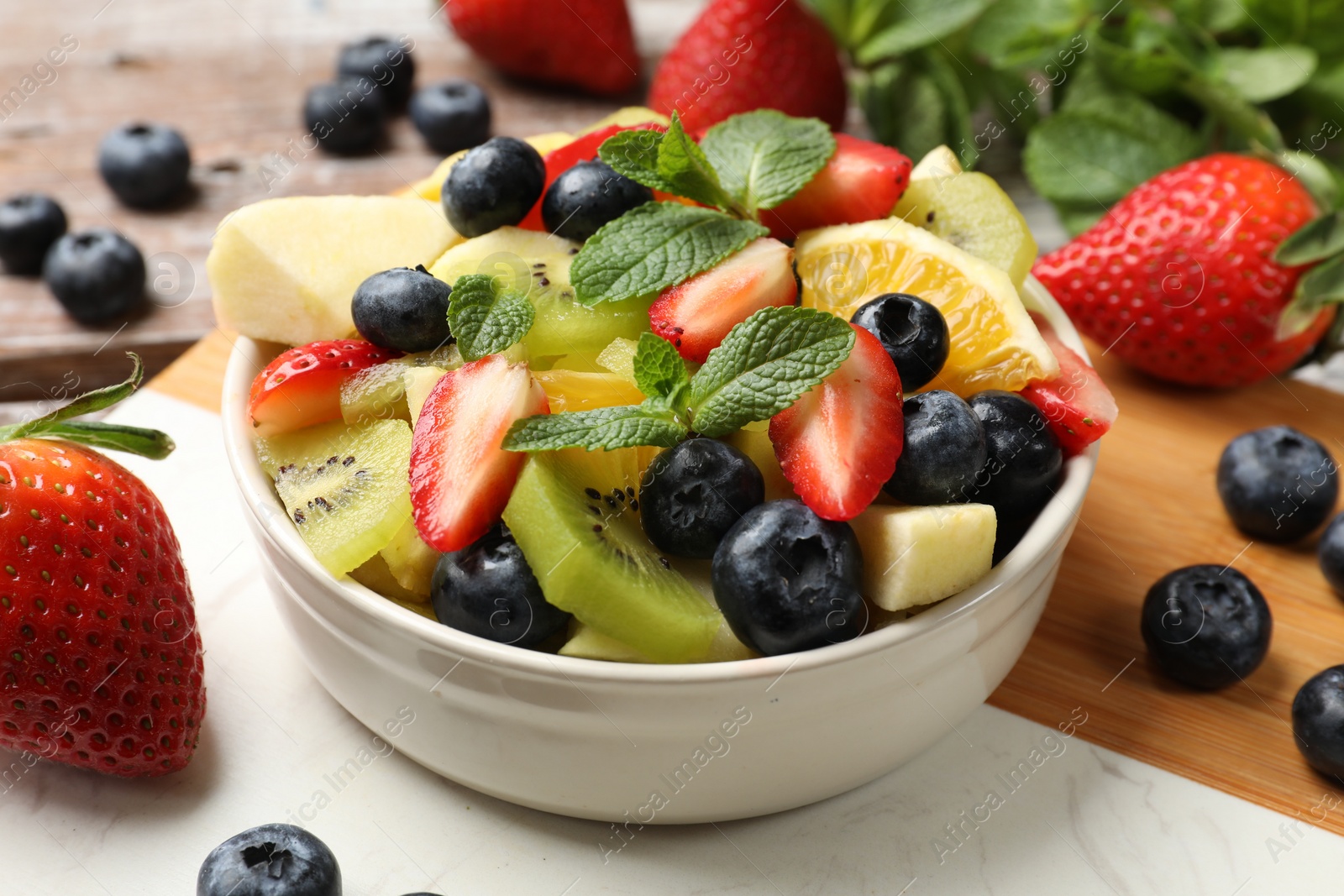 Photo of Tasty fruit salad in bowl and ingredients on wooden table, closeup