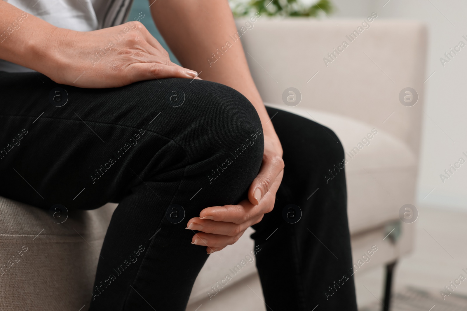 Photo of Woman suffering from knee pain on sofa indoors, closeup. Arthritis symptoms