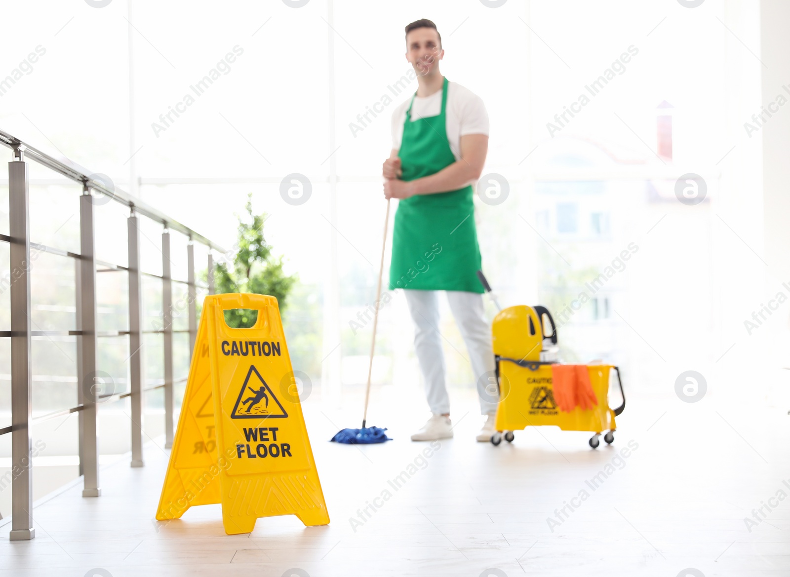 Photo of Safety sign with phrase "CAUTION WET FLOOR" and young man on background