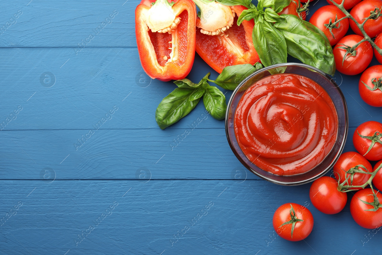 Photo of Bowl of tasty ketchup and ingredients on blue wooden table, flat lay. Space for text