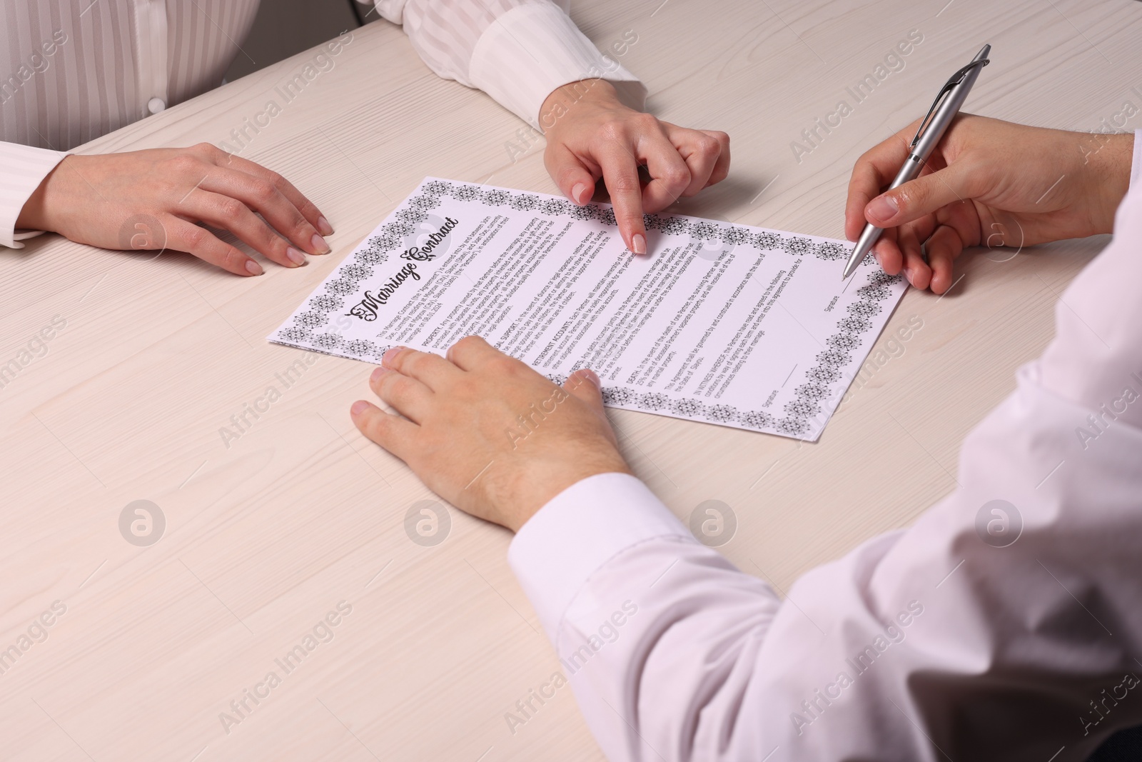 Photo of Man and woman signing marriage contract at light wooden table, closeup