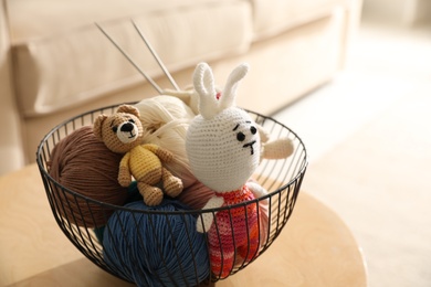 Photo of Basket with set of color threads and knitted toys on table indoors. Handicraft as hobby