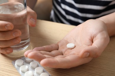 Man with glass of water and pill at wooden table, closeup