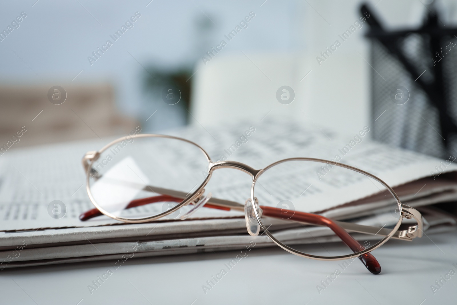 Photo of Stack of newspapers and glasses on white table indoors, closeup