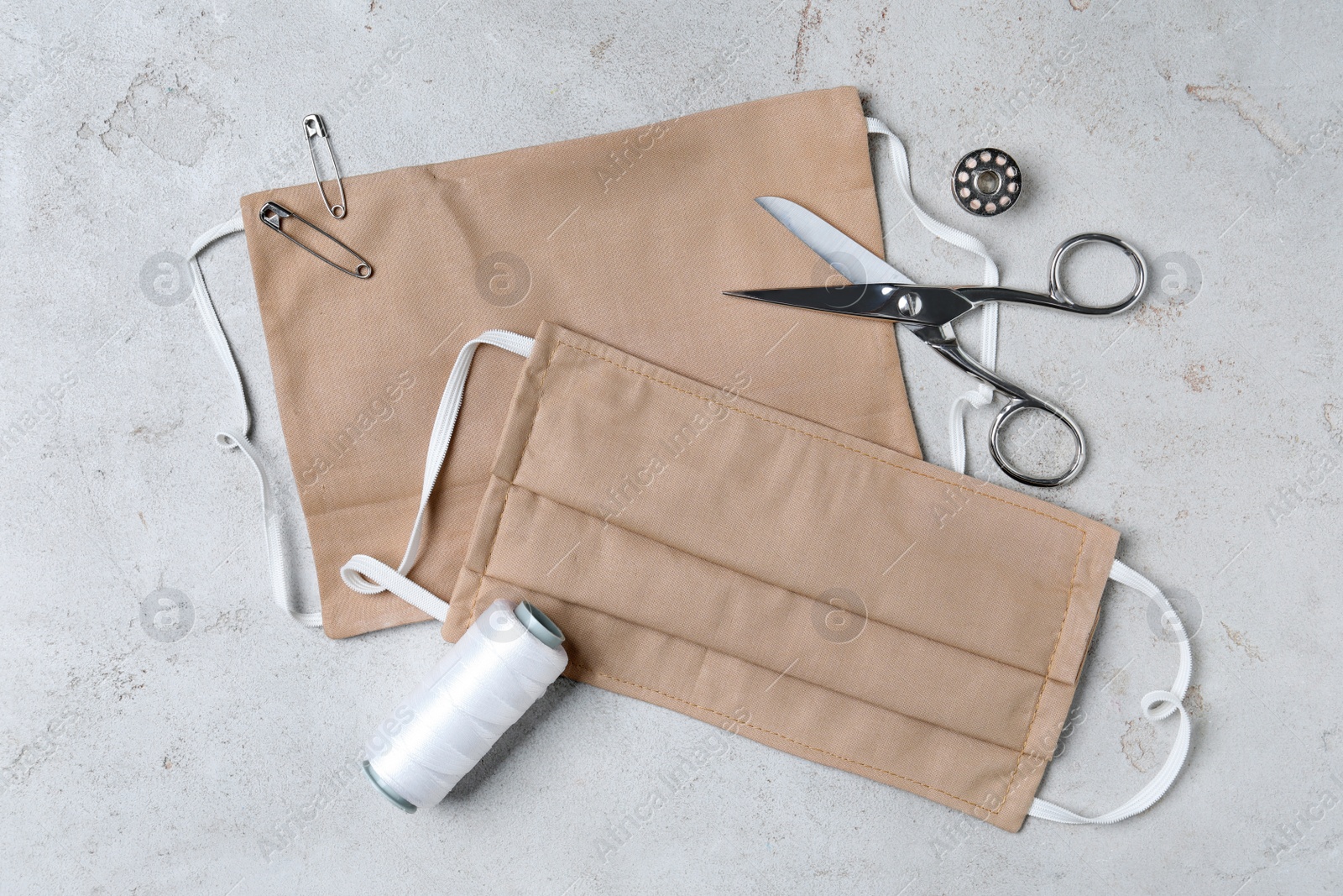 Photo of Homemade protective masks and sewing accessories on light grey stone background, flat lay