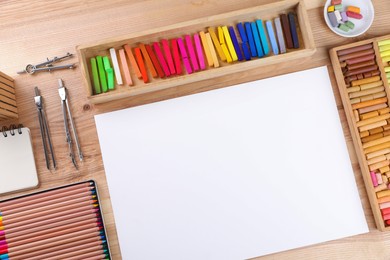 Layout with blank paper, soft pastels and other drawing supplies on wooden table at artist's workplace, top view. Space for design