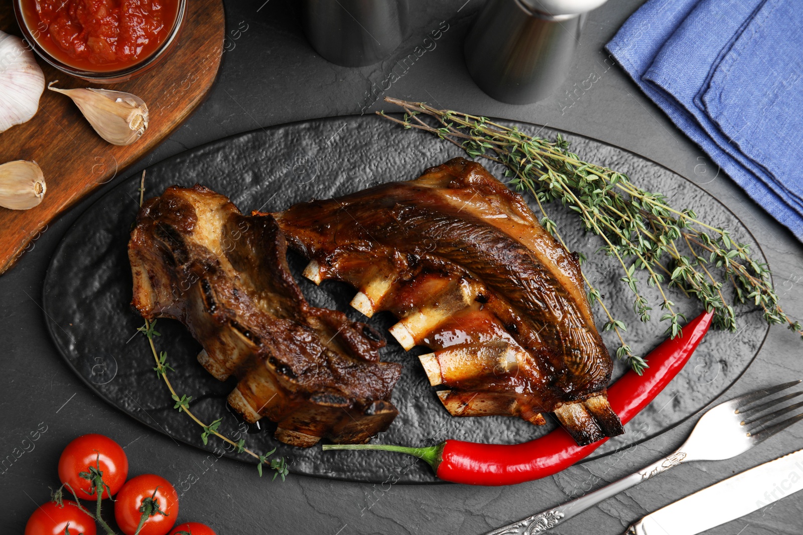 Photo of Delicious roasted ribs served on black table, flat lay