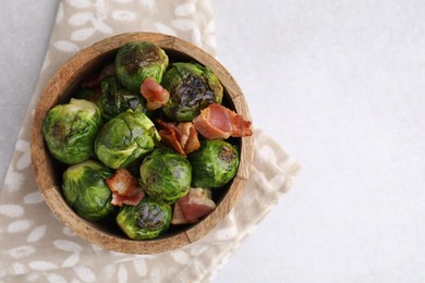 Photo of Delicious roasted Brussels sprouts and bacon in bowl on light table, top view. Space for text