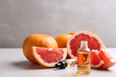 Bottle of essential oil and grapefruits on grey table, space for text