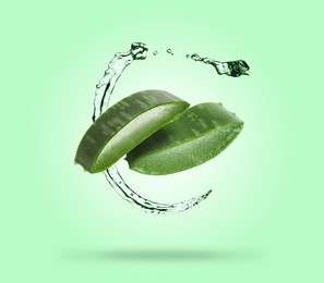Image of Sliced aloe vera leaf and splashes of juice on aquamarine background