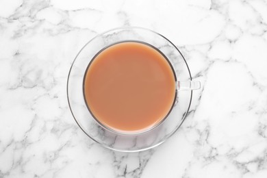 Photo of Delicious milk tea in glass cup on white marble table, top view