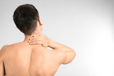 Young man suffering from neck pain on light background