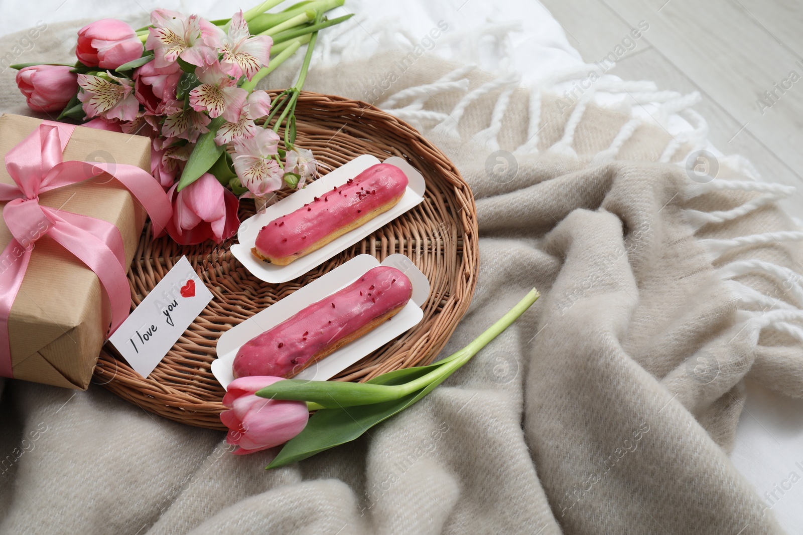 Photo of Tasty breakfast served in bed. Delicious eclairs, tea, flowers, gift box and card with phrase I Love You on blanket