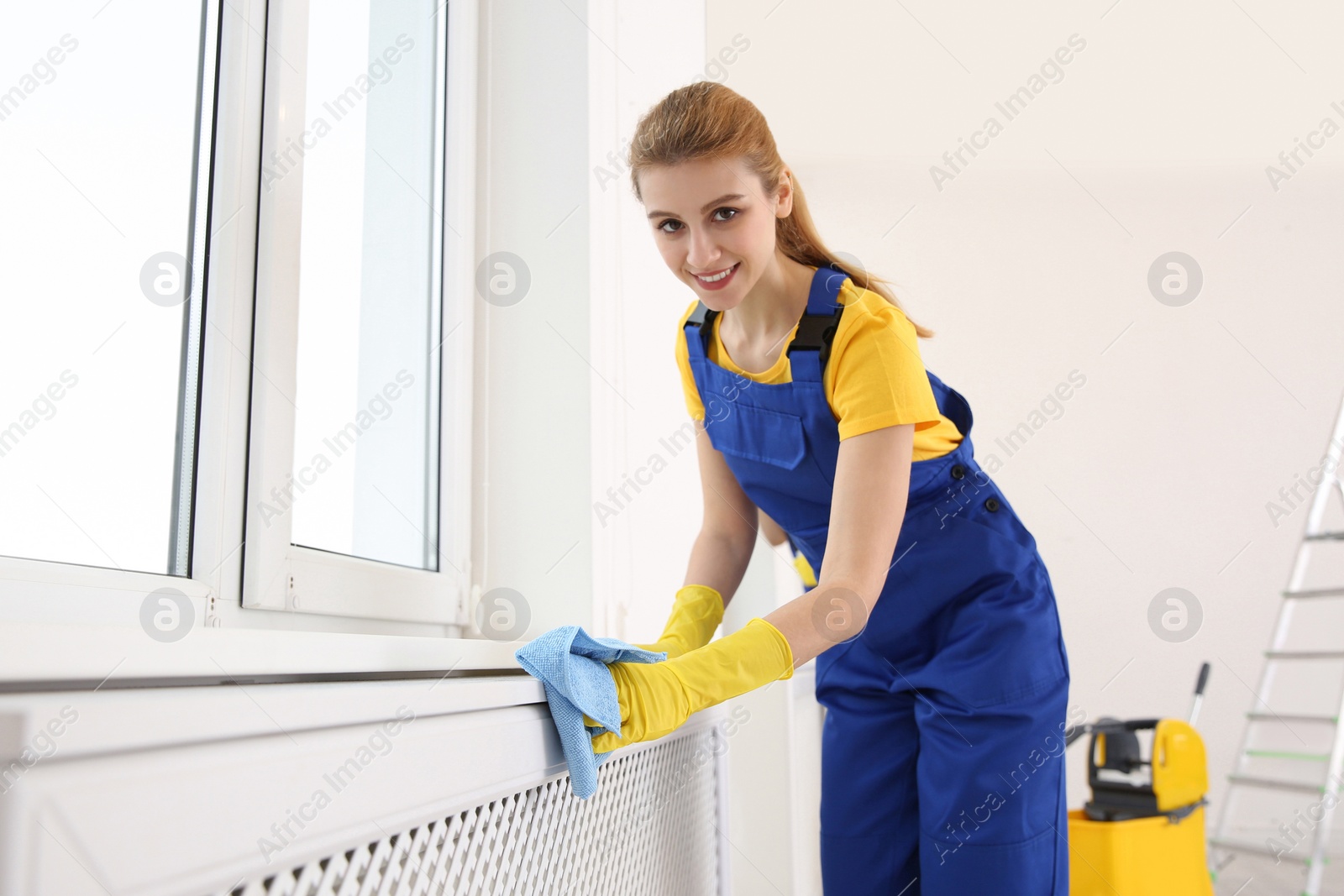 Photo of Professional young janitor cleaning windowsill in room