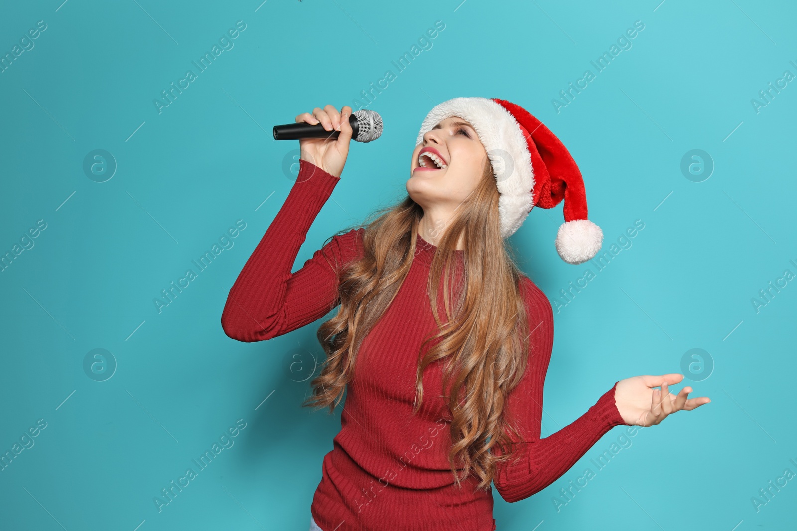 Photo of Young woman in Santa hat singing into microphone on color background. Christmas music