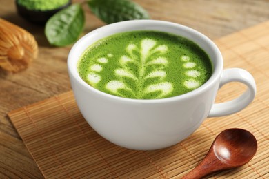 Photo of Delicious matcha latte in cup and spoon on wooden table, closeup