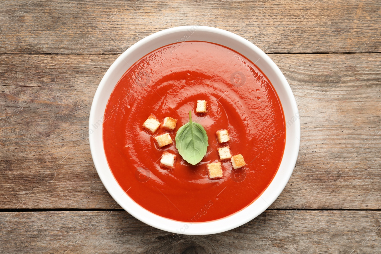 Photo of Bowl with fresh homemade tomato soup on wooden background, top view