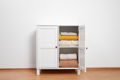 Photo of Wooden cabinet with clothes near white wall. Stylish furniture for wardrobe room