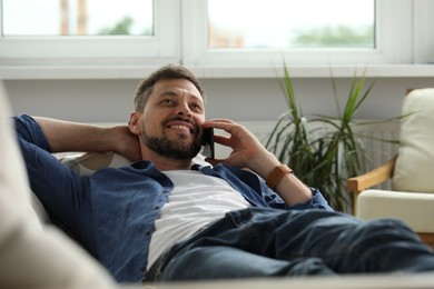Photo of Smiling man talking on smartphone at home