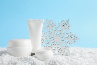 Set of winter skin care cosmetics with hand cream and decorative snowflake on snow against light blue background