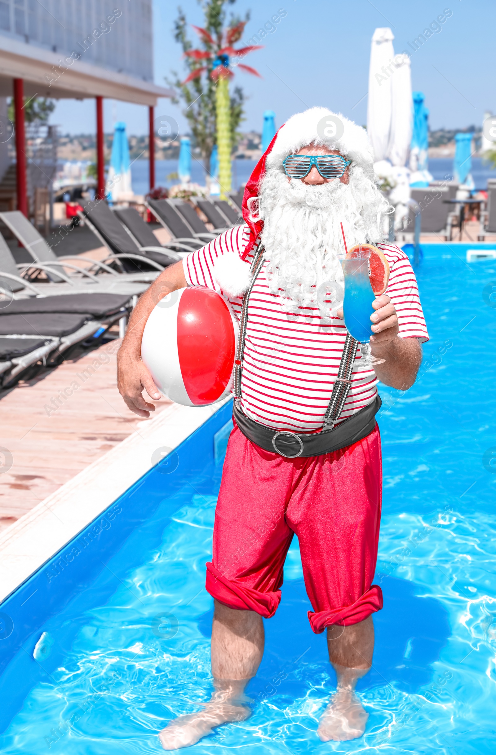 Photo of Authentic Santa Claus with cocktail and beach ball in pool at resort