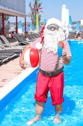 Authentic Santa Claus with cocktail and beach ball in pool at resort