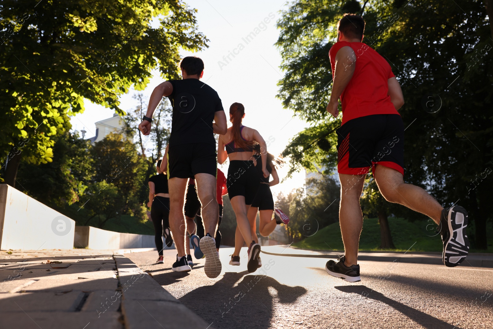 Photo of Group of people running outdoors on sunny day, back view