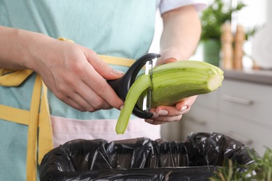 Woman peeling fresh zucchini above garbage bin indoors, closeup