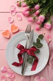 Photo of Place setting with heart shaped candles and bouquet of roses on pink wooden table, flat lay. Romantic dinner