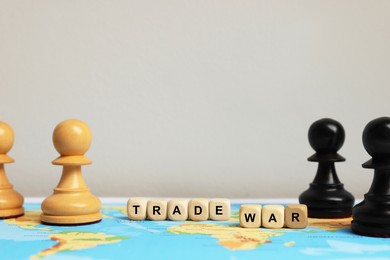 Photo of Wooden cubes with phrase Trade war and chess pieces on world map against light background