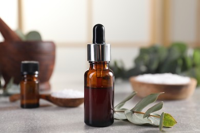 Aromatherapy. Bottle of essential oil and eucalyptus leaves on grey table