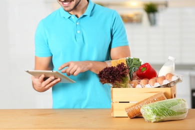 Photo of Young man with tablet PC and products in kitchen. Food delivery service