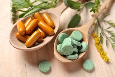 Different pills, herbs and flowers on wooden table, closeup. Dietary supplements