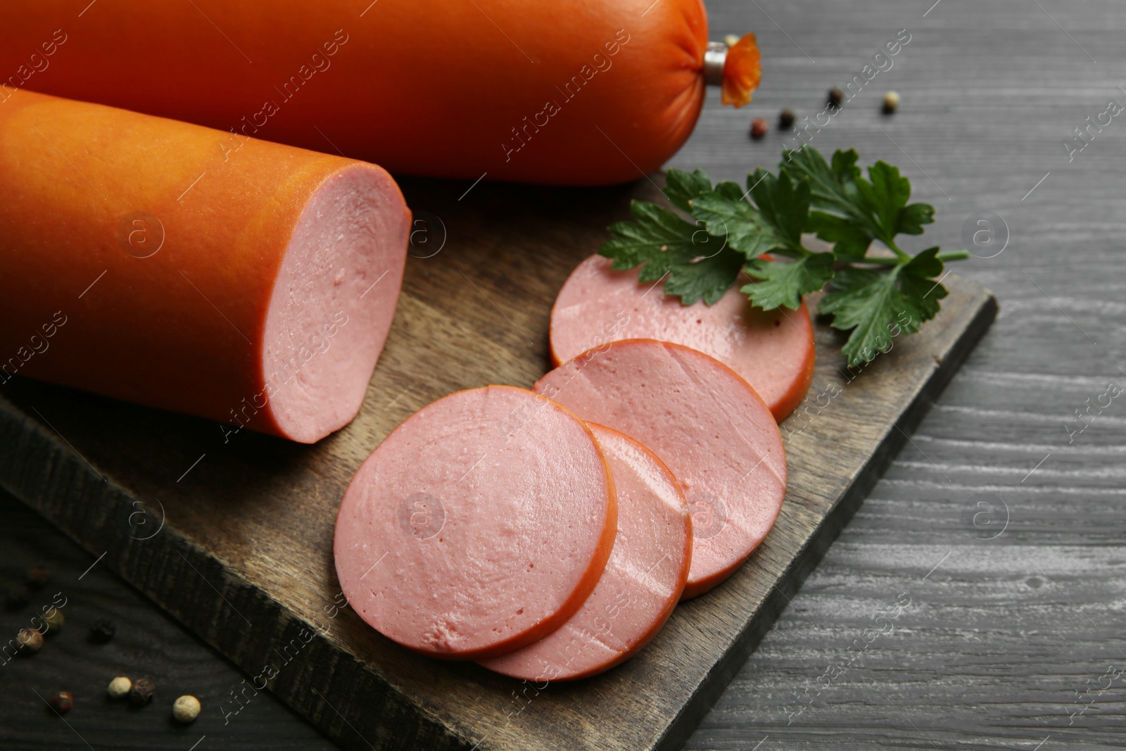 Photo of Board with tasty boiled sausages on dark wooden table, closeup