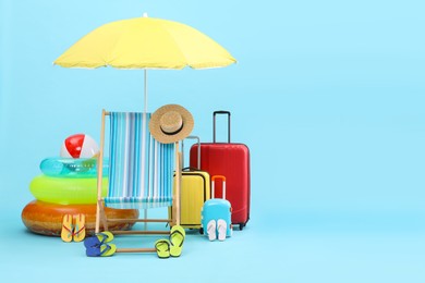 Photo of Deck chair, umbrella, suitcases and beach accessories on light blue background, space for text. Summer vacation