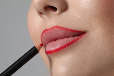 Photo of Young woman applying beautiful red lip pencil on grey background, closeup