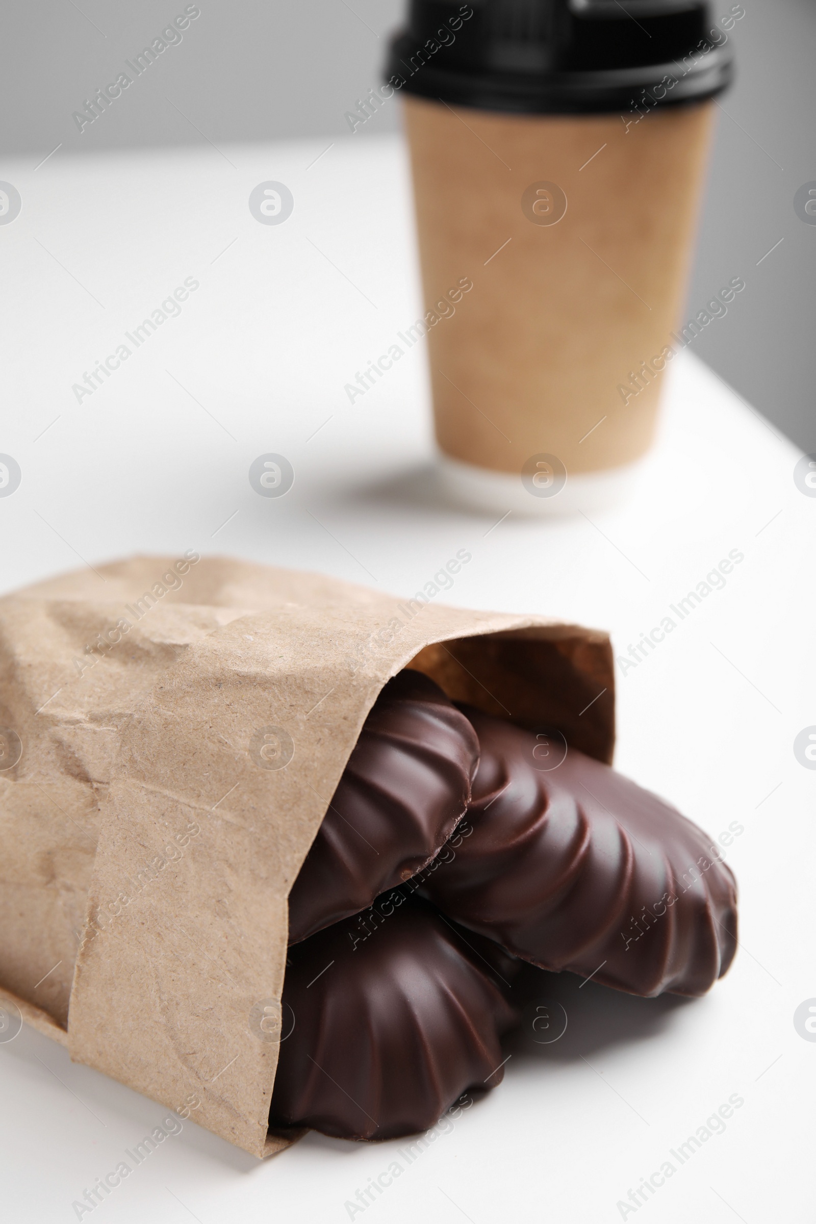 Photo of Delicious chocolate covered zephyrs in bag and paper cup on white table