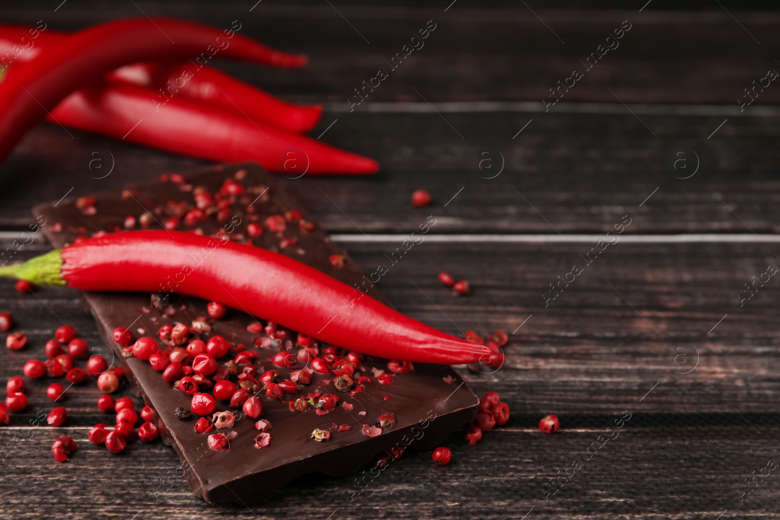 Photo of Delicious chocolate, fresh chili pepper and red peppercorns on wooden table, closeup. Space for text