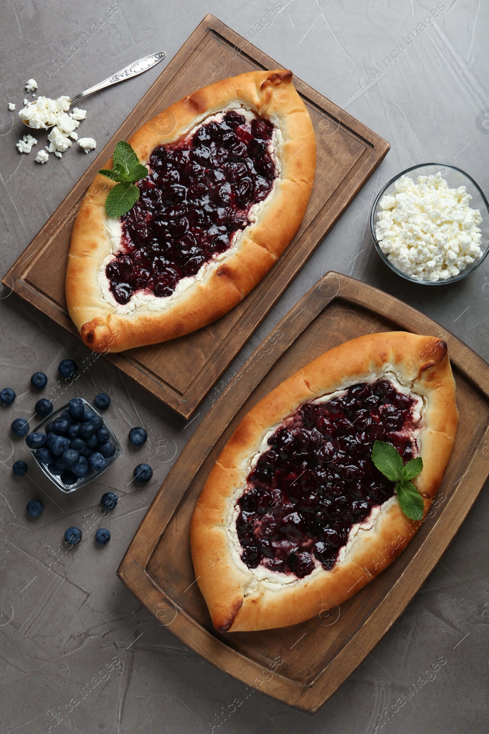 Photo of Delicious sweet cottage cheese pastry with cherry jam and fresh blueberries on grey table, flat lay