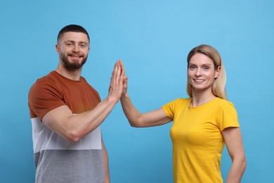 Photo of Happy couple giving high five on light blue background