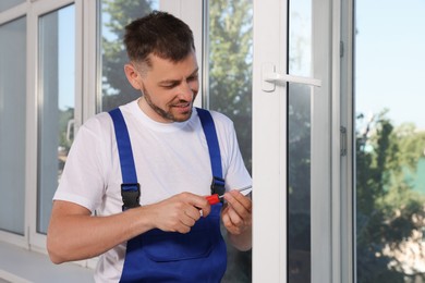 Photo of Worker adjusting installed window with screwdriver indoors