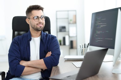 Photo of Happy young programmer working with laptop in office