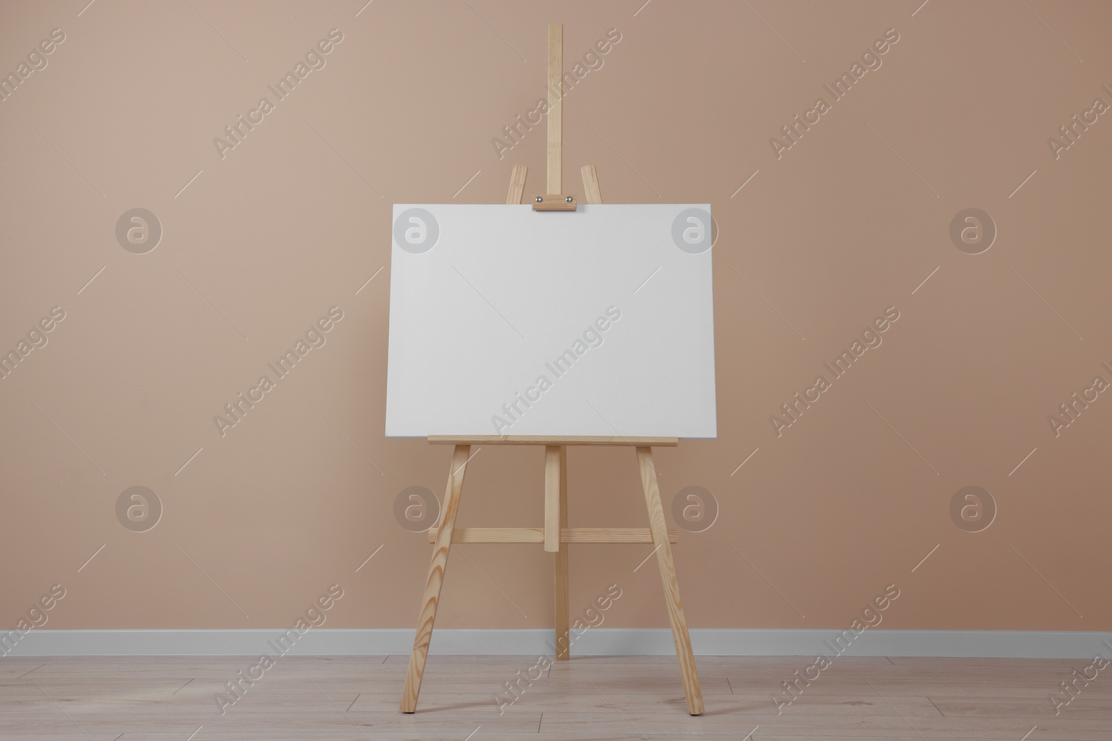 Photo of Wooden easel with blank canvas near beige wall indoors.