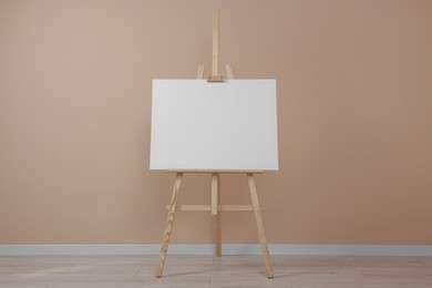 Wooden easel with blank canvas near beige wall indoors.